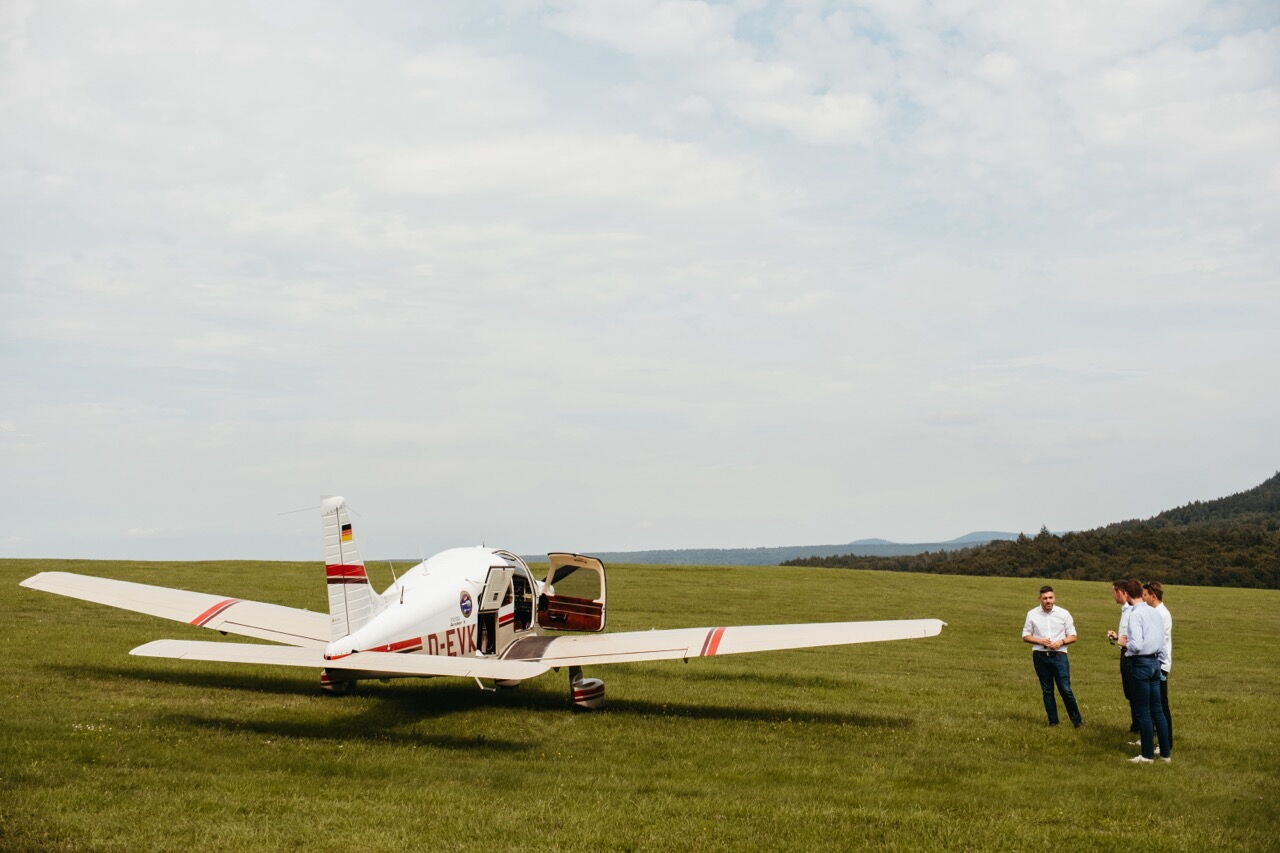Konstantin Kuhle in conversation with pilots next to a small sports aircraft on a green meadow.