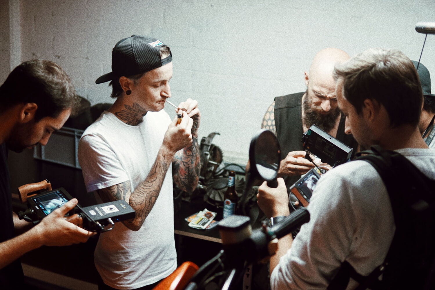 Filmcrew und tätowierte Protagonisten der Berliner Motorrad-Szene in einer Werkstatt, während sich einer eine Zigarette anzündet.