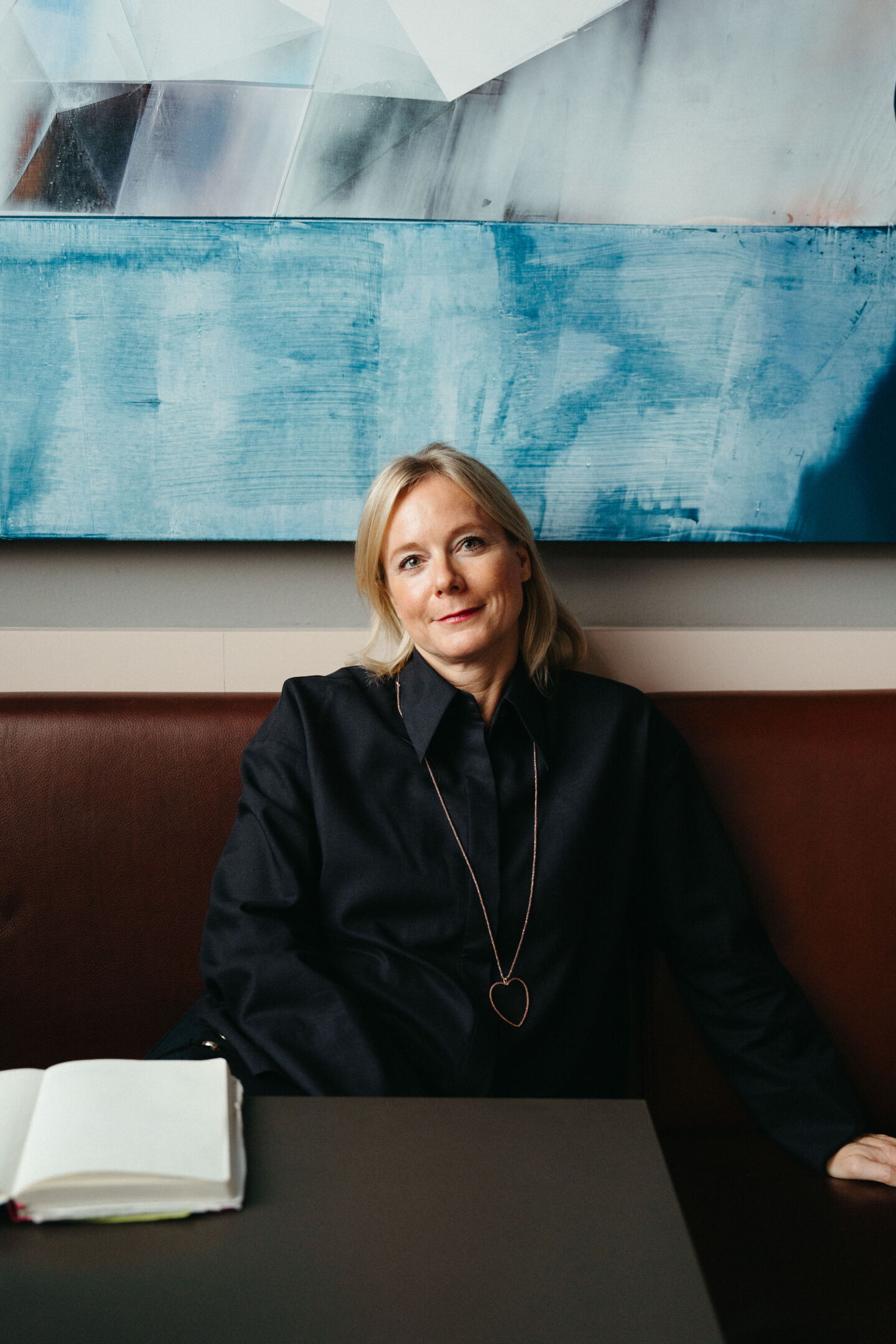 Nina Pütz smiling in front of a blue abstract painting at Rutz Berlin. Personal branding photography by Munir Werner.