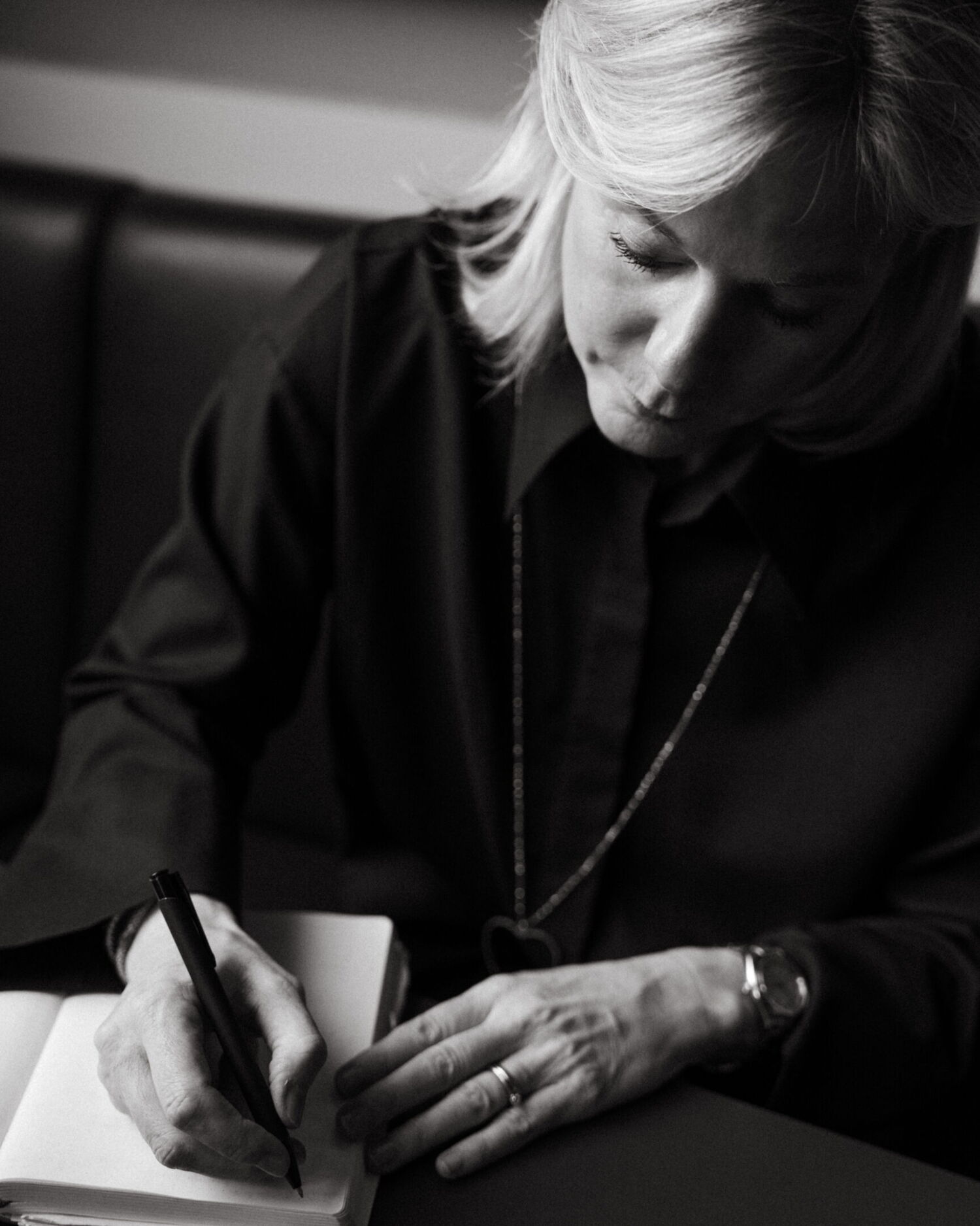 Black and white portrait of Nina Pütz writing thoughtfully in a notebook. Business photography at Rutz Berlin by Munir Werner.