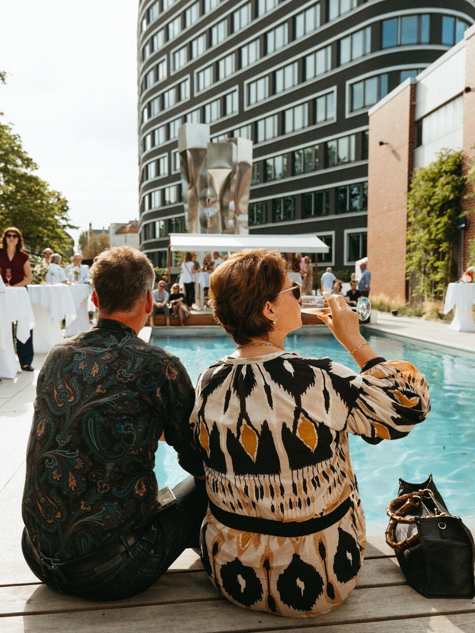 Guests enjoying wine by the poolside at an event on the EUREF-Campus, overlooking modern architecture and sculptures.