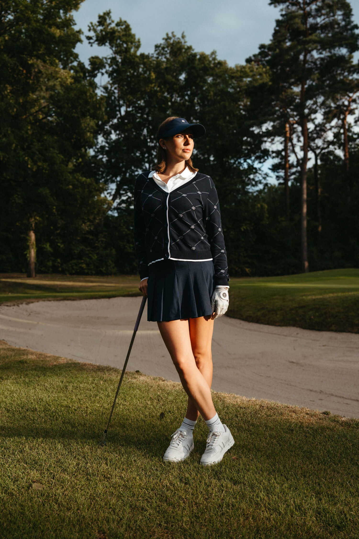 Laura Kowohl posing relaxed on the fairway, leaning on her club, showcasing a navy blue Röhnisch golf outfit with a skirt.