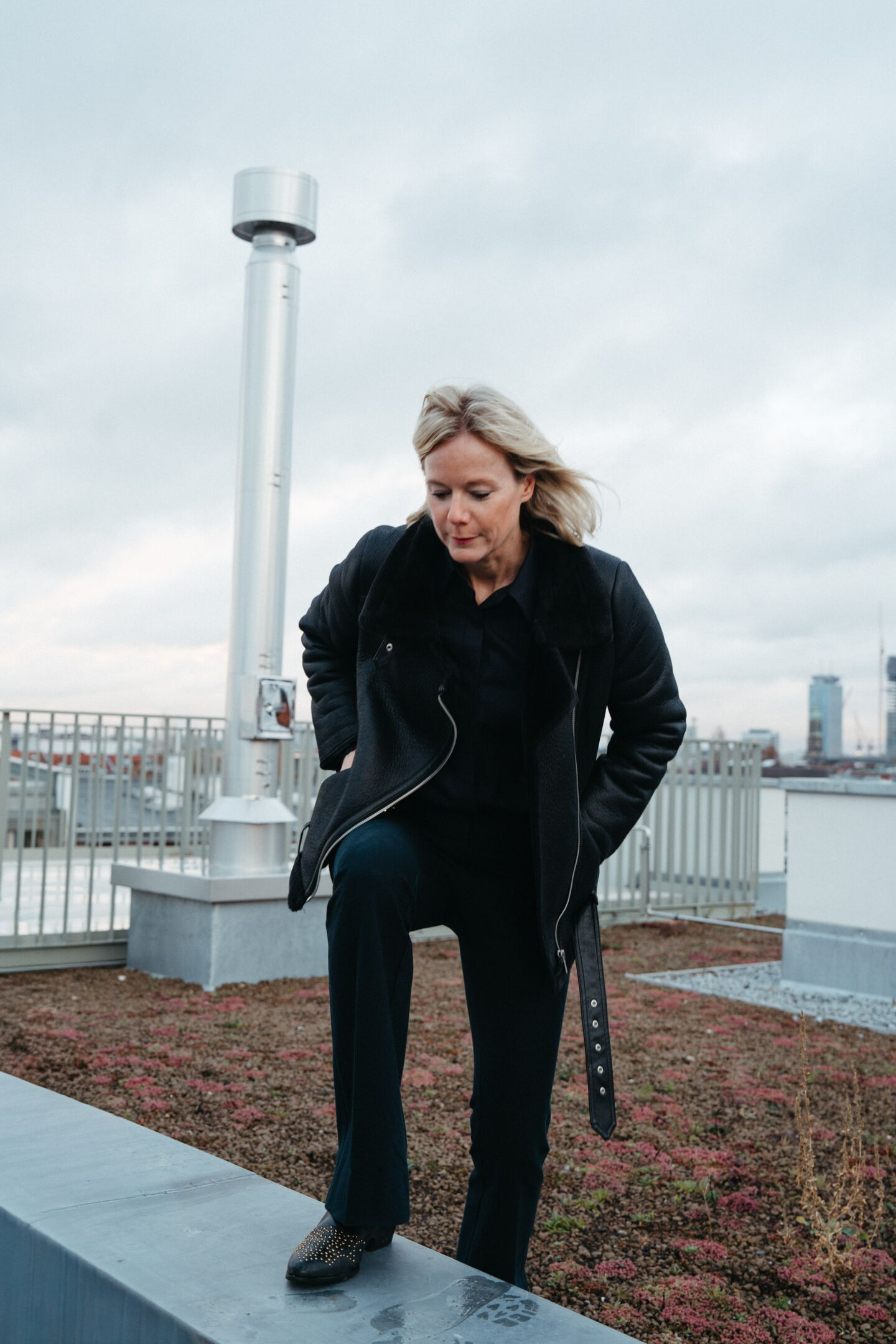 Nina Pütz, CEO of parfumdreams and Niche Beauty, stepping confidently onto a ledge with the Berlin skyline in the background. Dynamic personal branding portrait by Munir Werner.