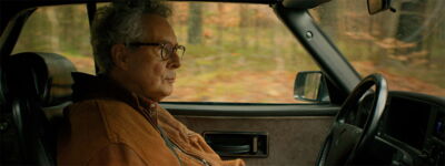 Side profile of the protagonist driving a classic black Saab convertible through an autumnal forest, scene from the brand film.
