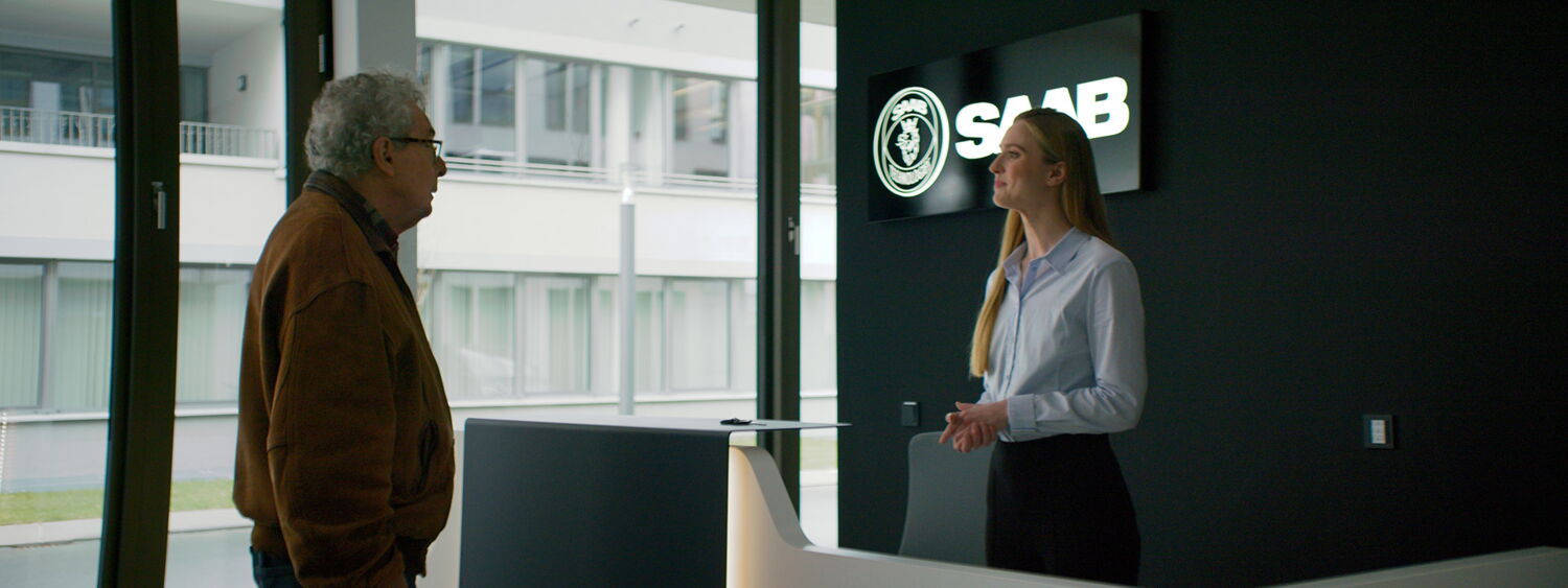 A friendly Saab employee at the reception explaining the company's actual focus on defense technology to the visitor.