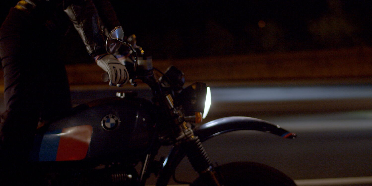 Cinematic detail shot while riding: Hand on the handlebars and the tank of a BMW bike at night with motion blur.