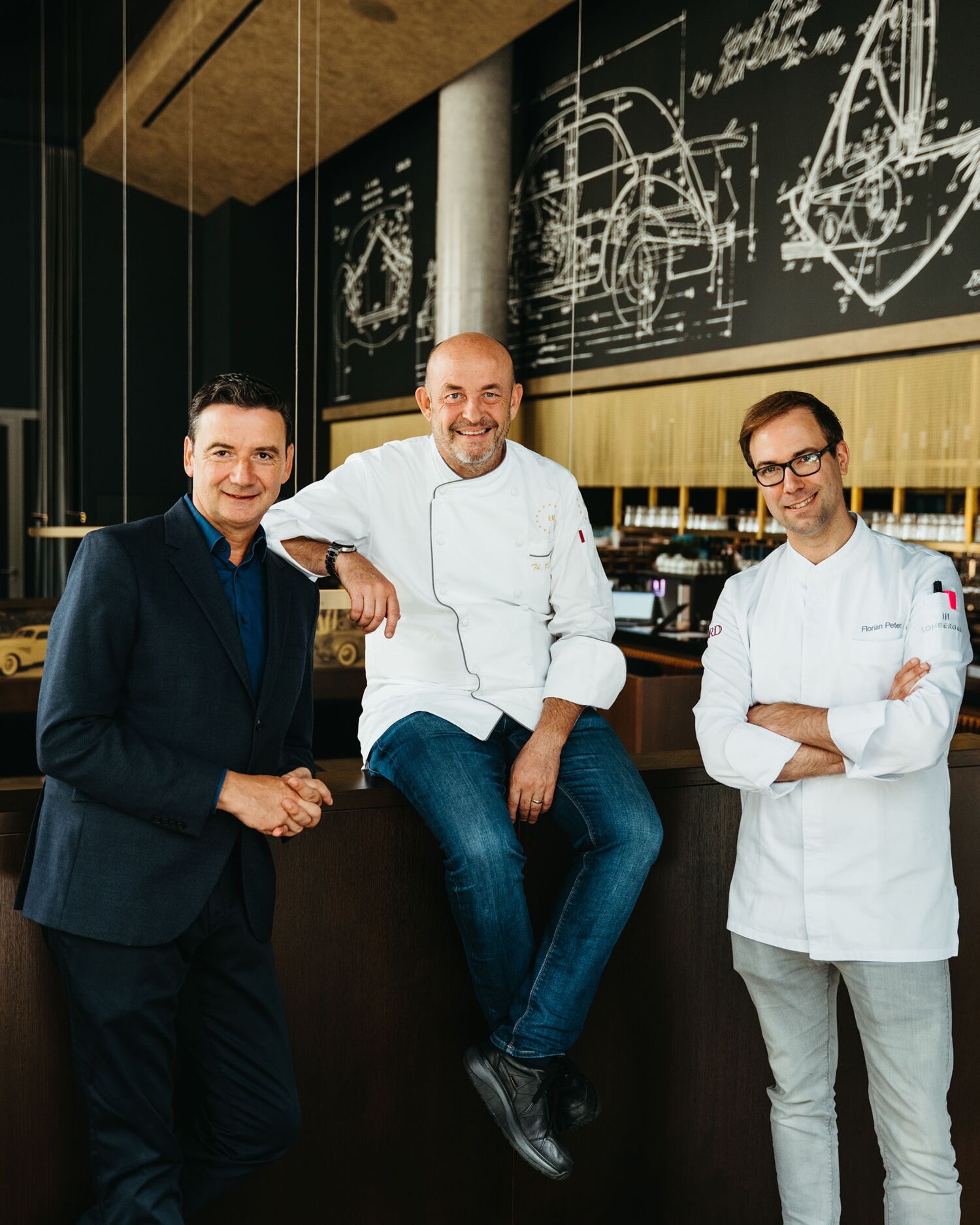 The restaurant's leadership team, consisting of the manager and two head chefs, posing relaxed and smiling in front of a wall with technical drawings.