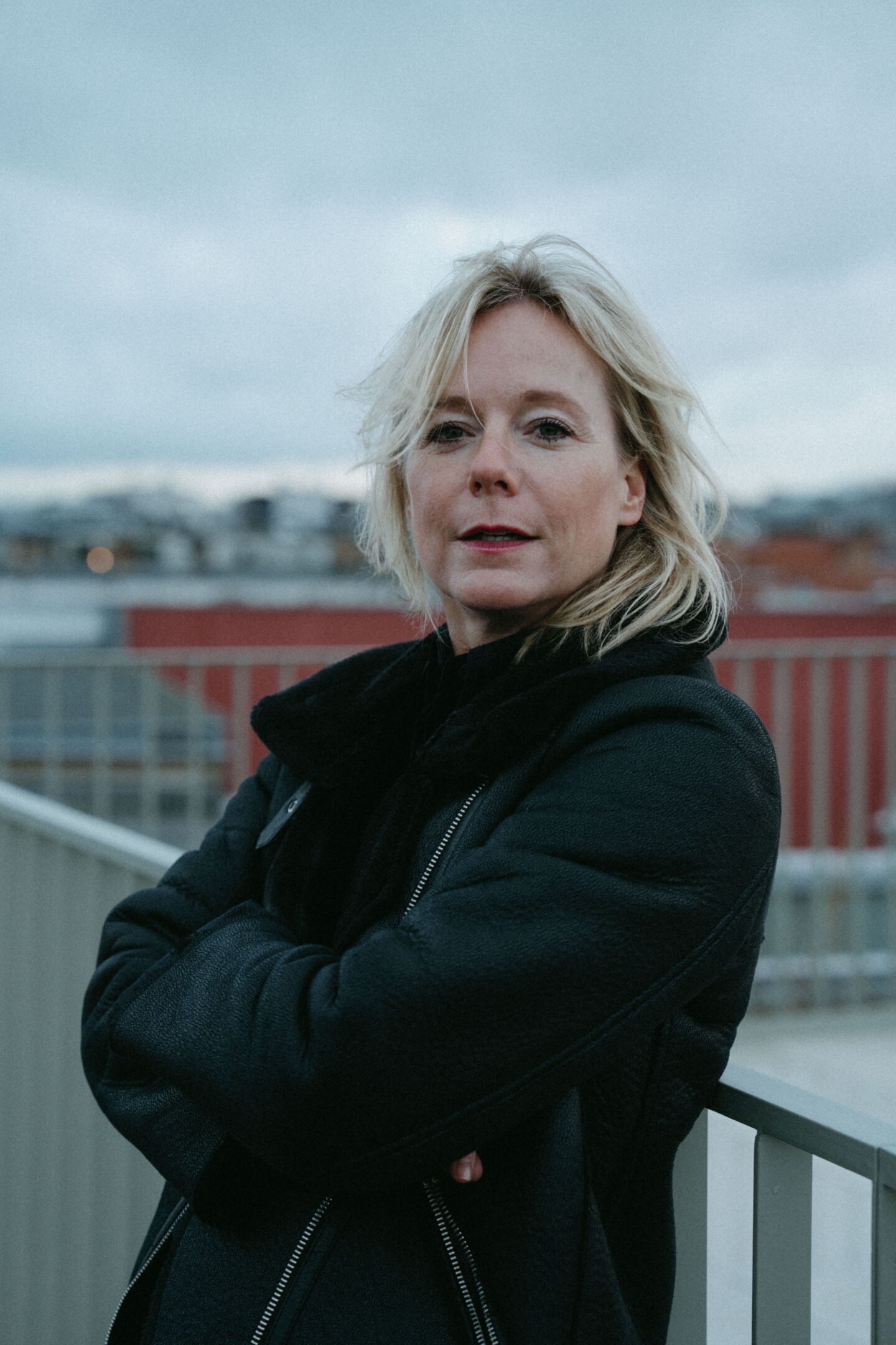 Nina Pütz standing confidently in a black jacket with crossed arms on a Berlin rooftop. Personal branding portrait by Munir Werner.