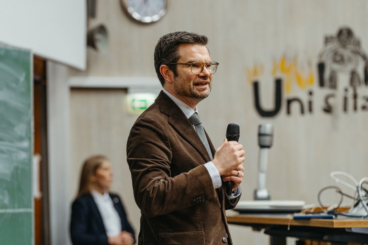 Marco Buschmann giving a speech in a university lecture hall, engaging in dialogue with students about education and politics.