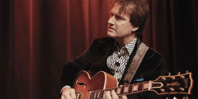 Jazz guitarist Oliver Doering focused on playing his Gibson guitar in front of a red stage curtain. Preview for the film's visual cutdown.