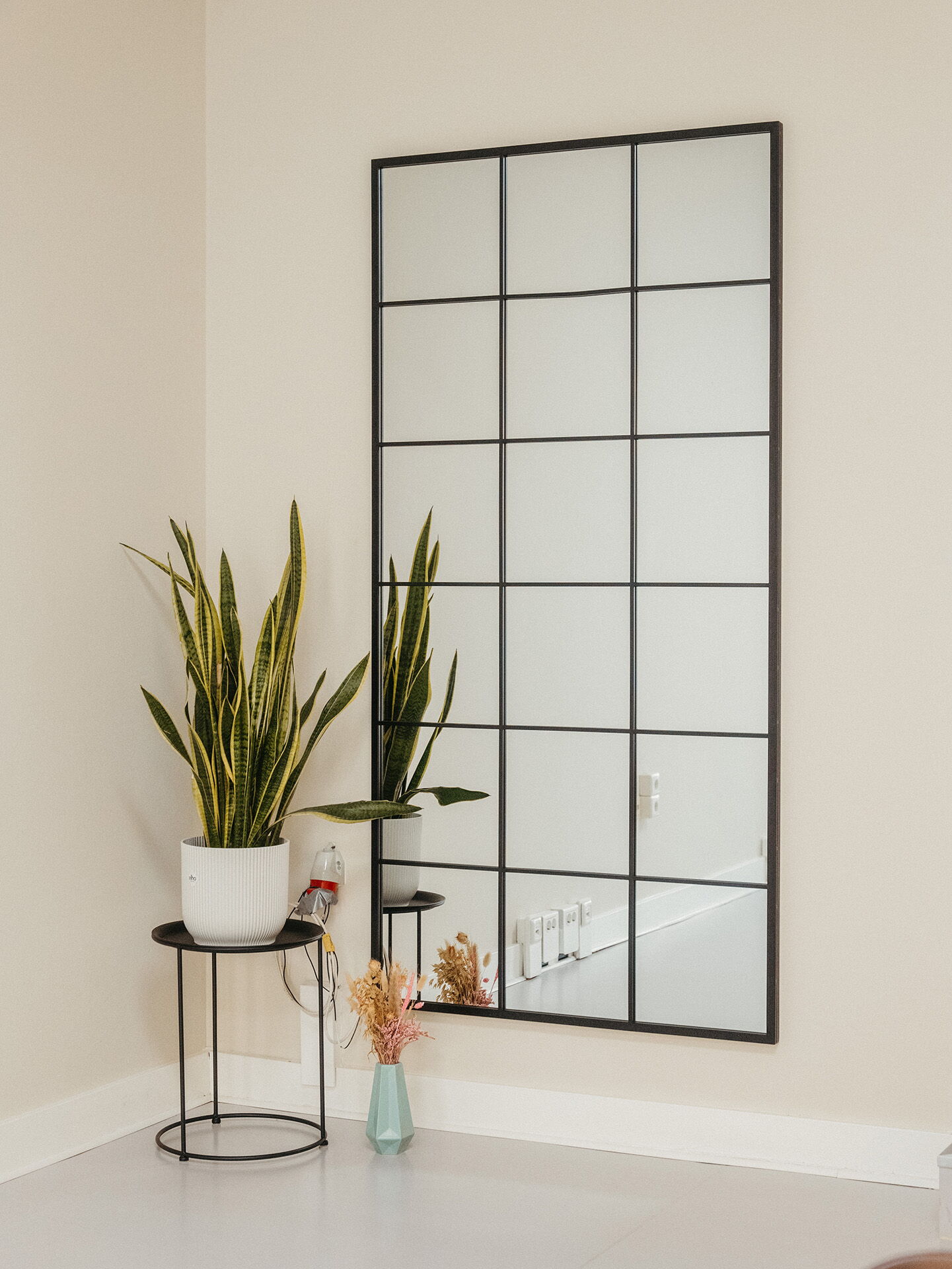 A large, black-framed industrial-style mirror leaning against the wall next to a snake plant, reflecting the spaciousness of the Visionary Berlin and Munir Werner rental studio.