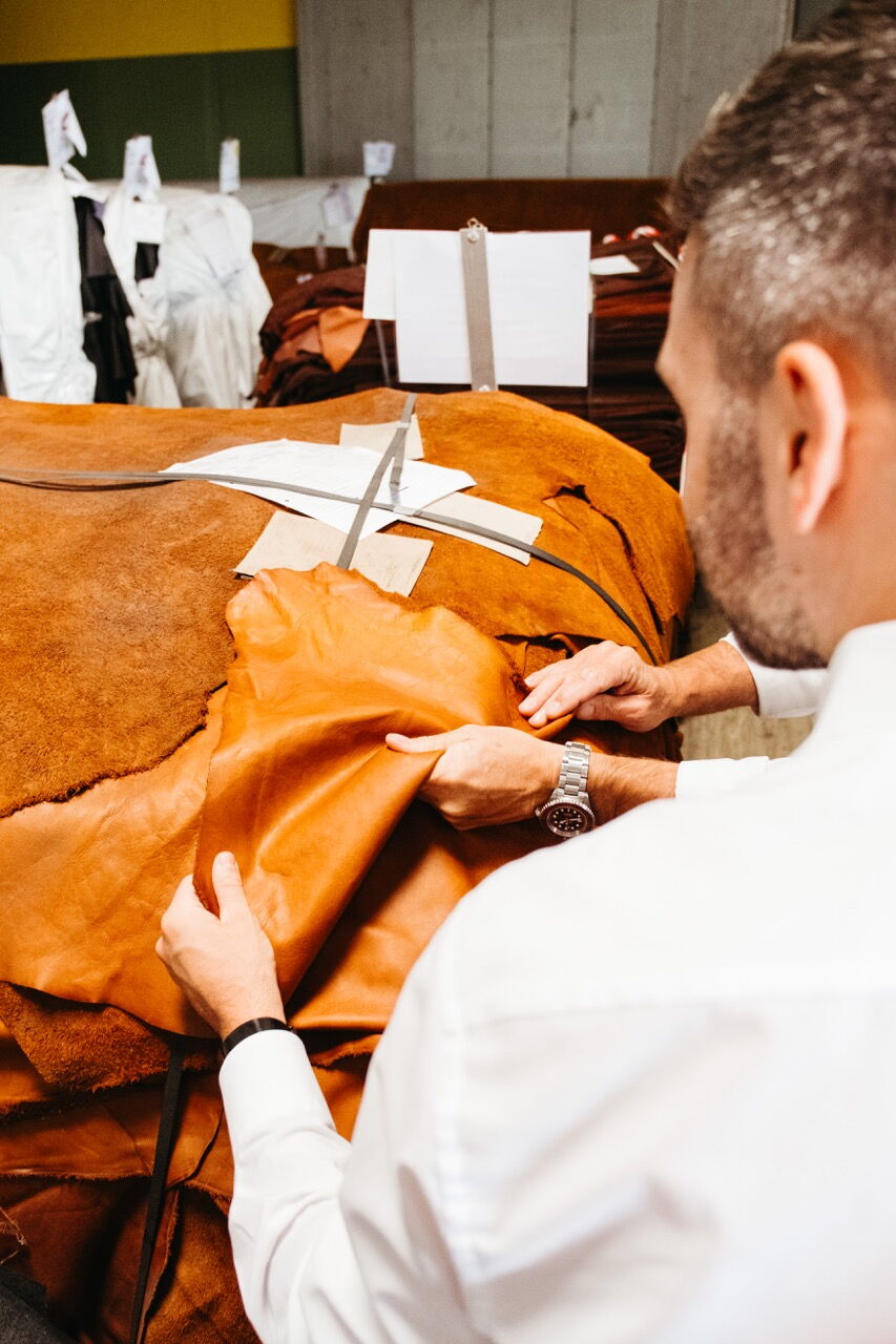 Close-up shot: Hands checking the texture and quality of a brown leather hide during production.