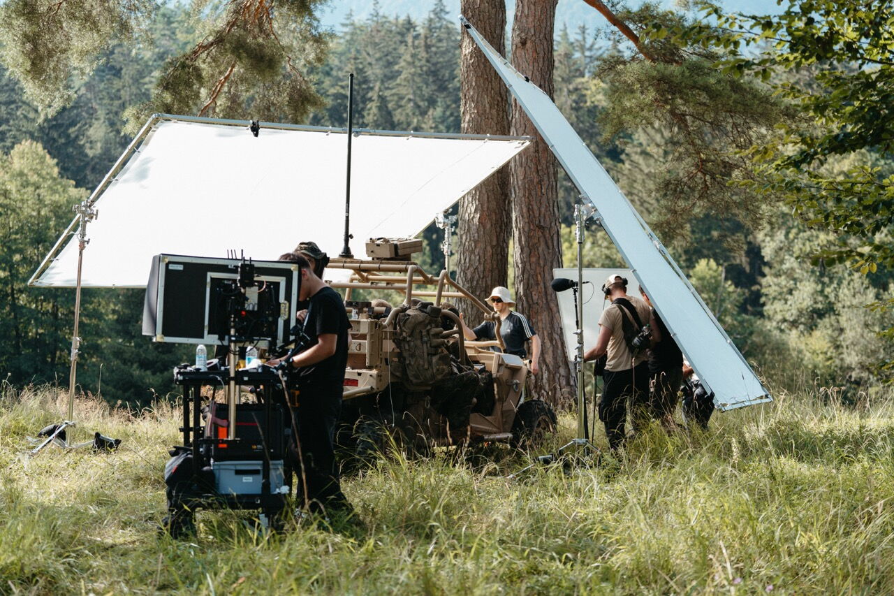 Filmcrew beim Aufbau eines großen Lichtsegels (Butterfly) neben einem militärischen Buggy für den Saab L20C Produktfilm im Wald.