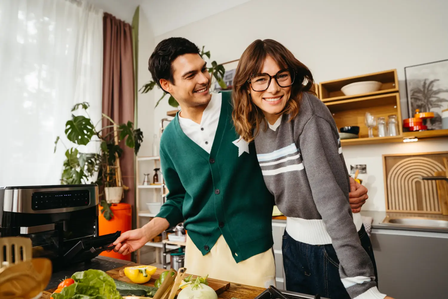 A happy couple laughing together in the kitchen while preparing vegetables. Lifestyle commercial aesthetic shot by Munir Werner and Felix Julian Koch..