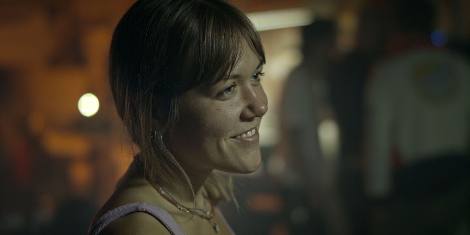 Close-up of a smiling young woman from the Berlin motorcycle scene bathed in warm, cinematic light.