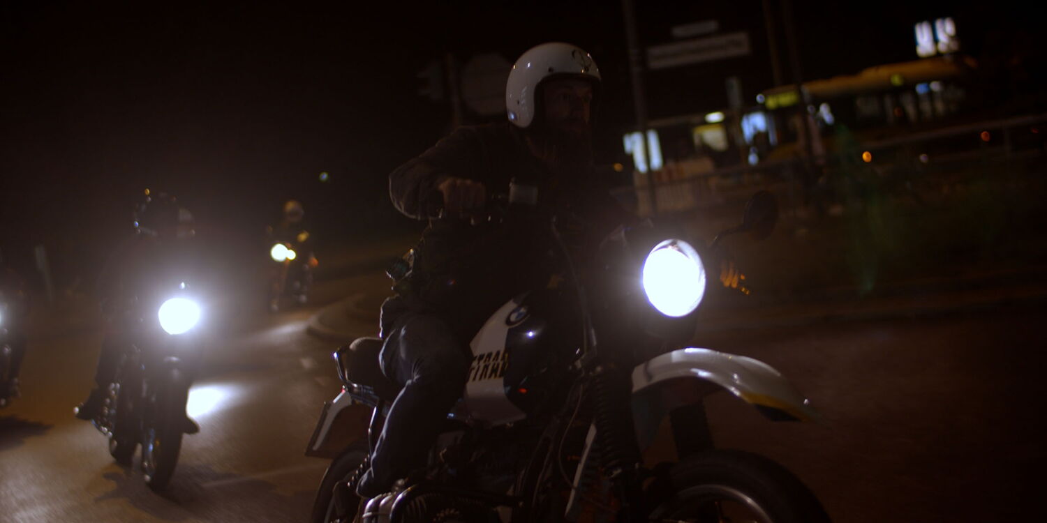 A group of motorcyclists riding through Berlin at night, captured with headlights beaming into the camera for a cinematic look.