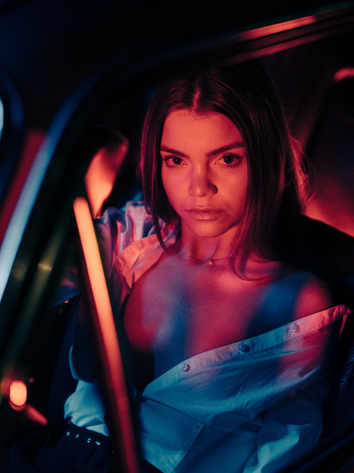 Intense fashion portrait inside a car interior, showcasing the model with strong red light and deep shadows (chiaroscuro).