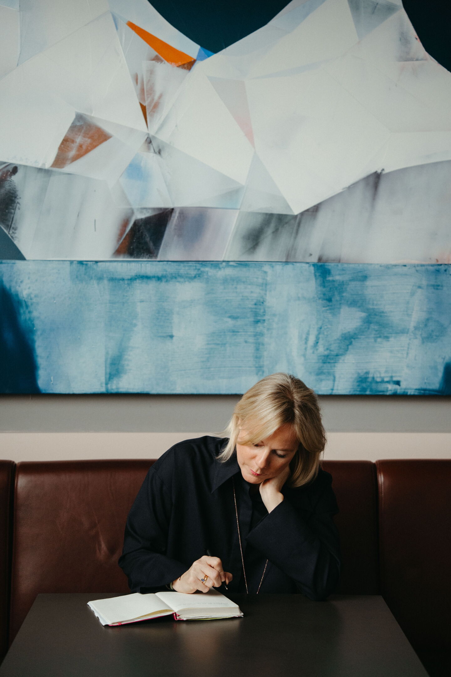 Nina Pütz sitting thoughtfully with a pen at a table in Rutz Berlin. Personal branding photography by Munir Werner.