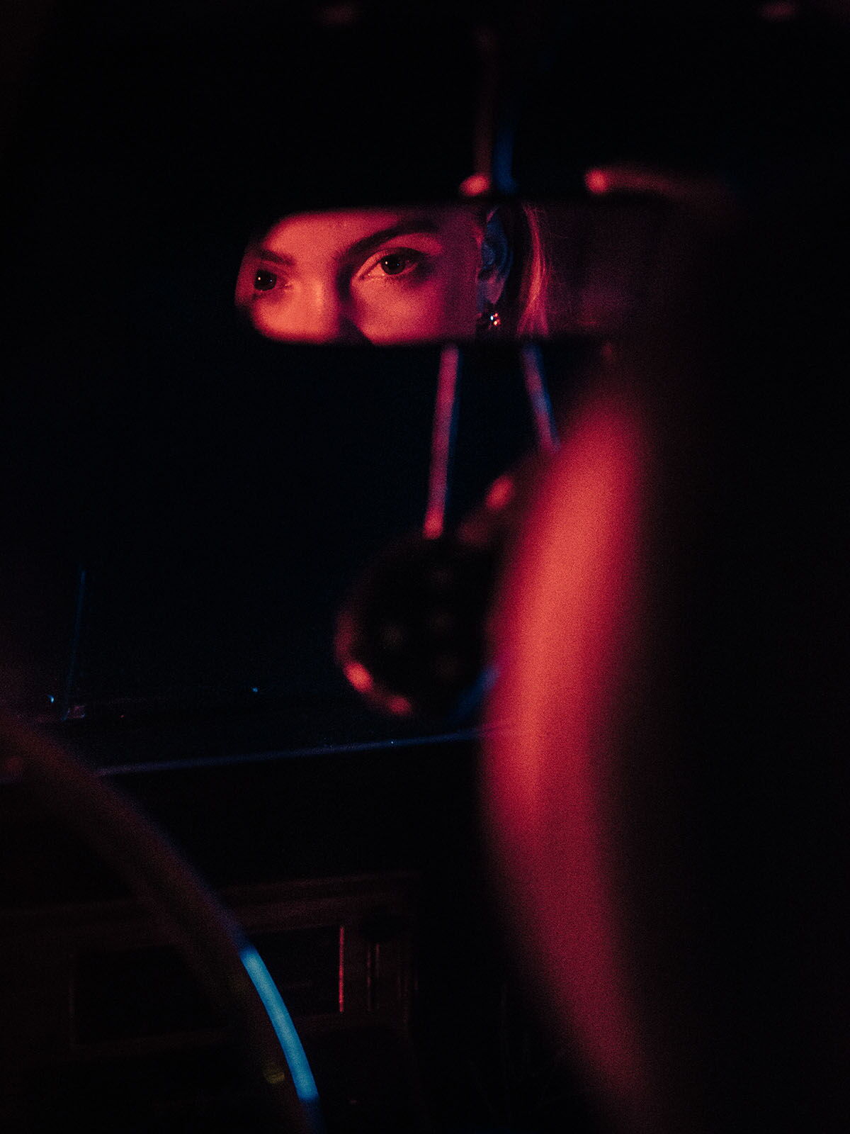 A woman's eyes intensely reflected in a car's rearview mirror, captured in a dark, cinematic noir atmosphere.