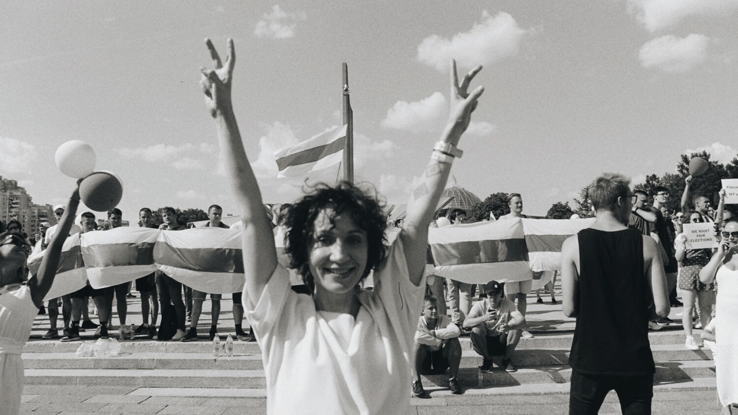 Black and white shot of a woman showing victory signs in front of the white-red-white flag during the protests in Belarus.