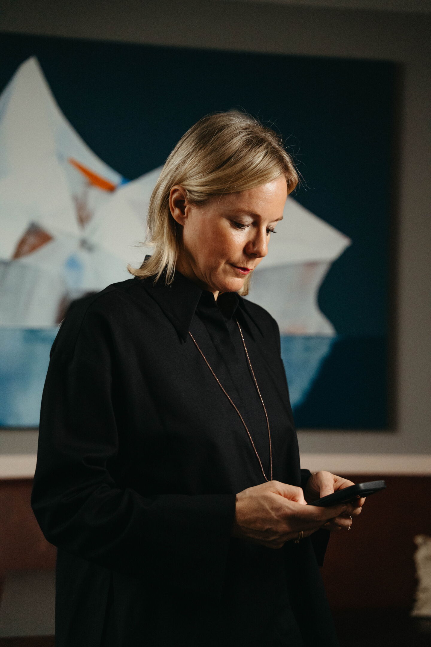 Nina Pütz checking her smartphone in front of a blue artwork at Rutz Berlin. Authentic CEO portrait by Munir Werner.