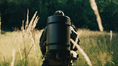 Rear view of a soldier carrying the Saab Sirius Compact L20C system as a manpack through tall grass in the forest.