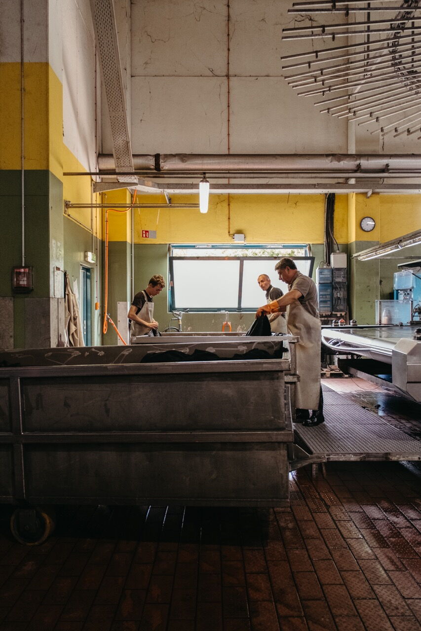 Workers processing heavy leather hides at large industrial vats in a tannery.