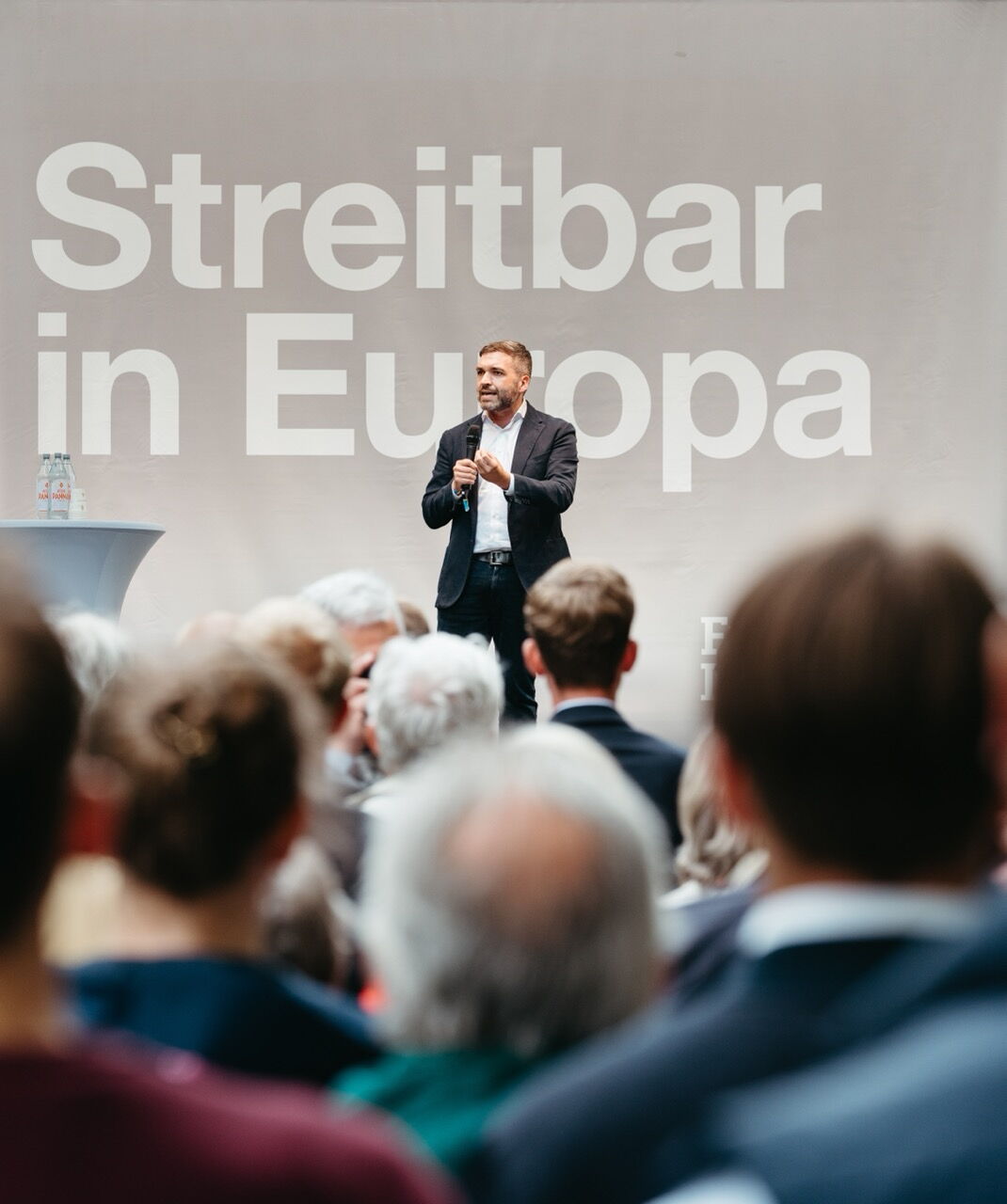 Konstantin Kuhle speaking with a microphone to an audience on stage with the backdrop "Streitbar in Europa" – a moment of political debate.