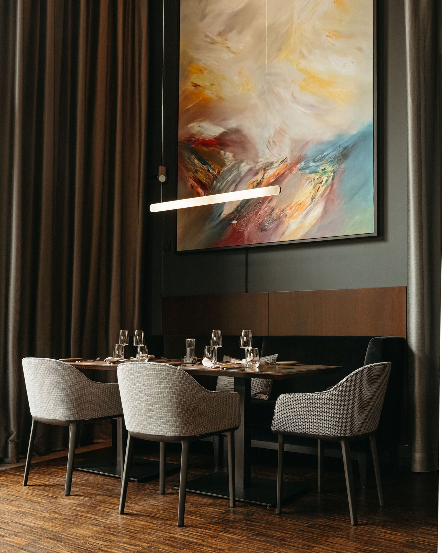 Interior of the fine-dining restaurant featuring a large abstract painting, modern pendant lighting, and set tables against a dark wall.