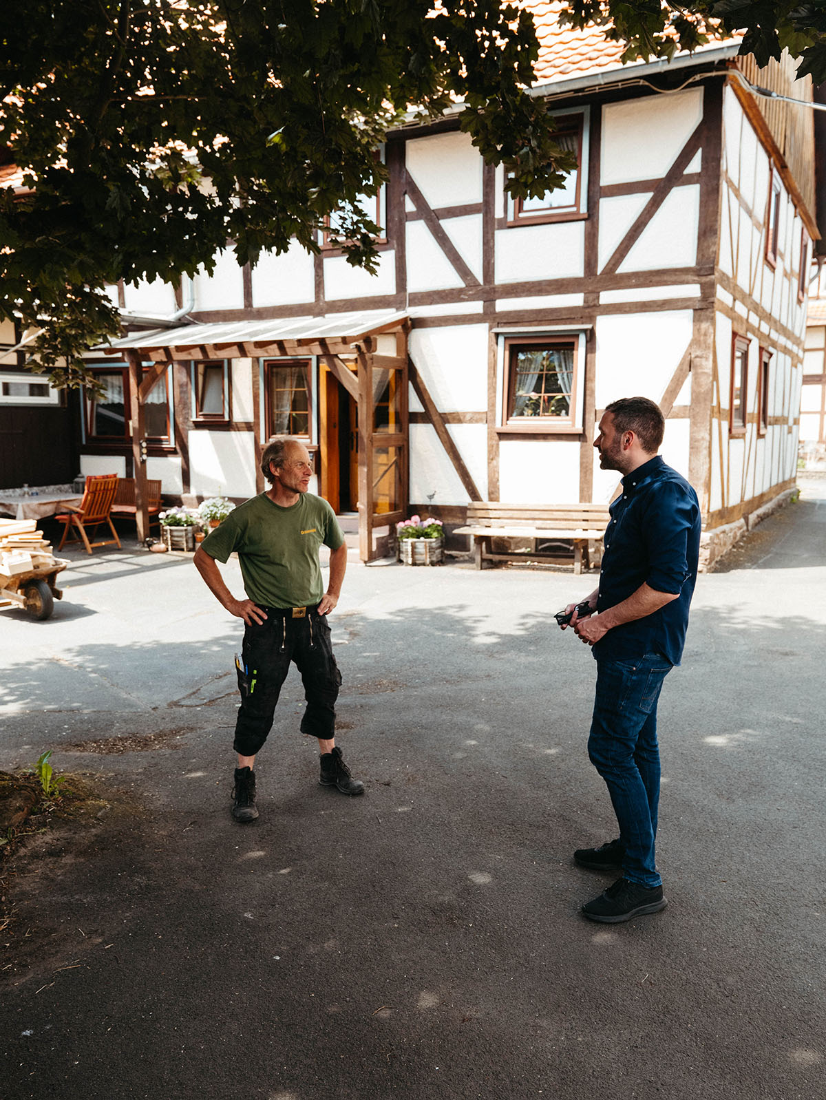 Konstantin Kuhle in conversation with a carpenter in front of a traditional half-timbered house.