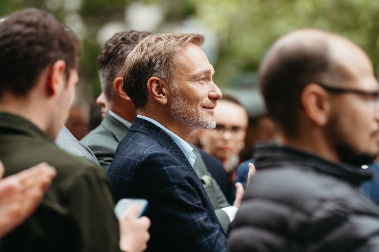 Seitenprofil von Christian Lindner im Publikum einer politischen Veranstaltung, aufmerksam und lächelnd zuhörend.