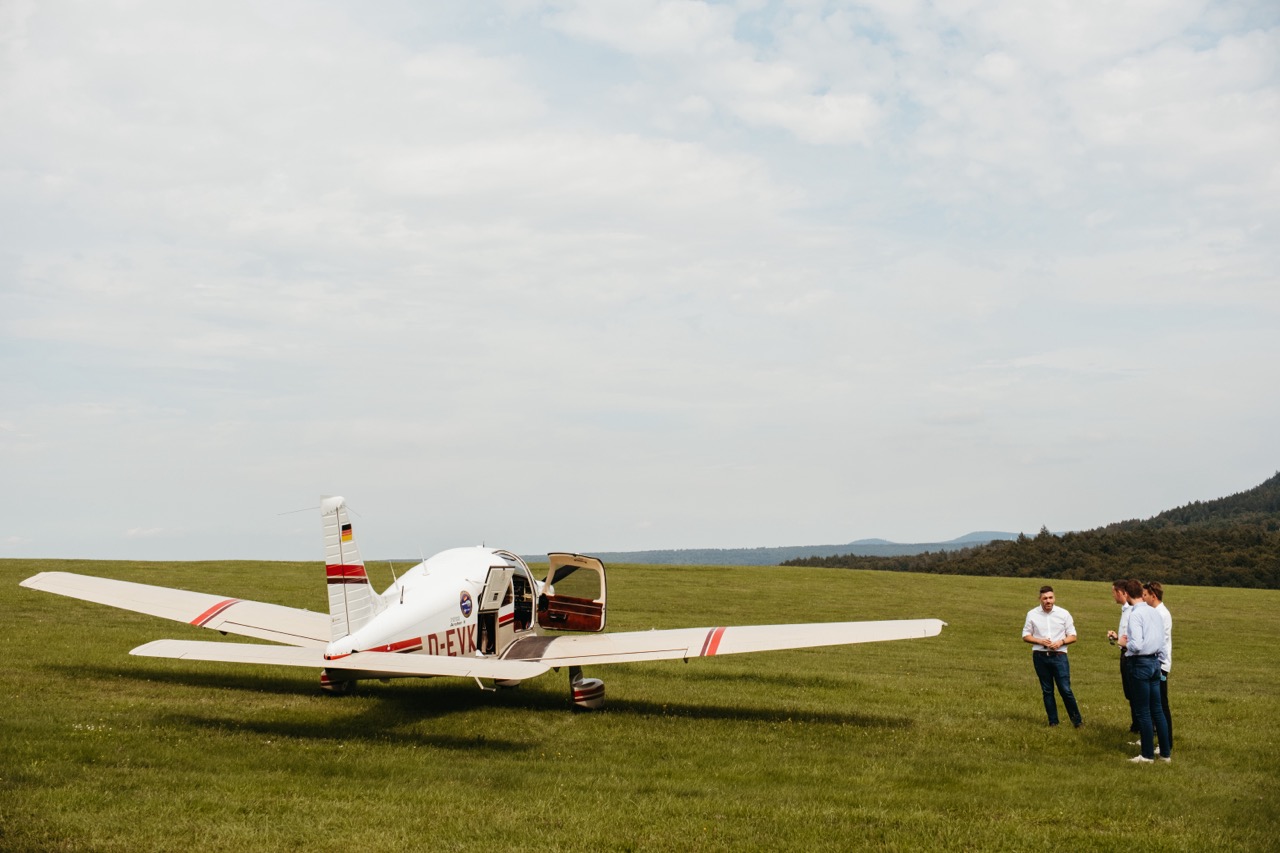 Konstantin Kuhle im Gespräch mit Piloten neben einem kleinen Sportflugzeug auf einer grünen Wiese.