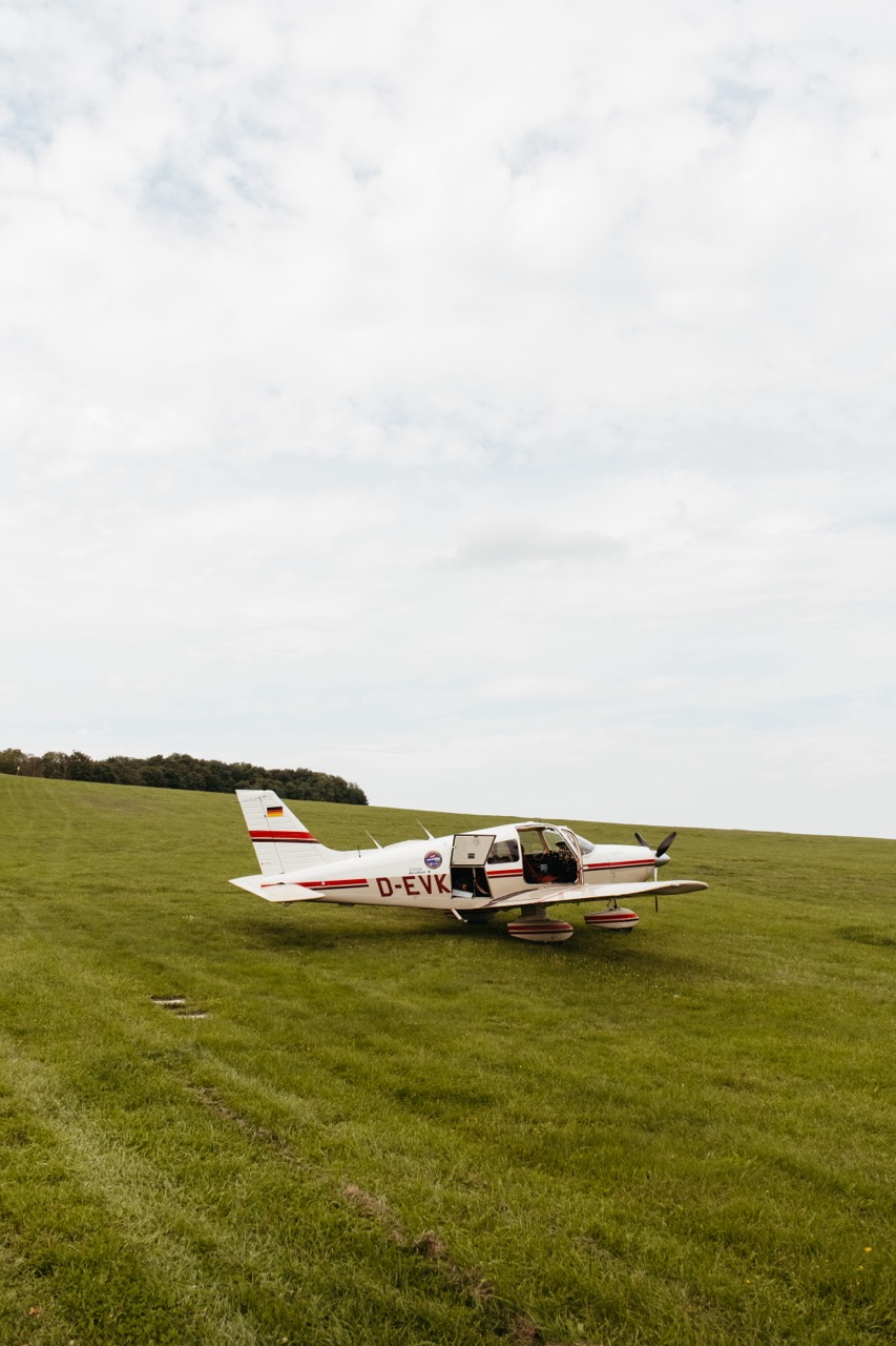 Ein kleines Sportflugzeug steht mit offener Tür auf der Landebahn eines ländlichen Flugplatzes.